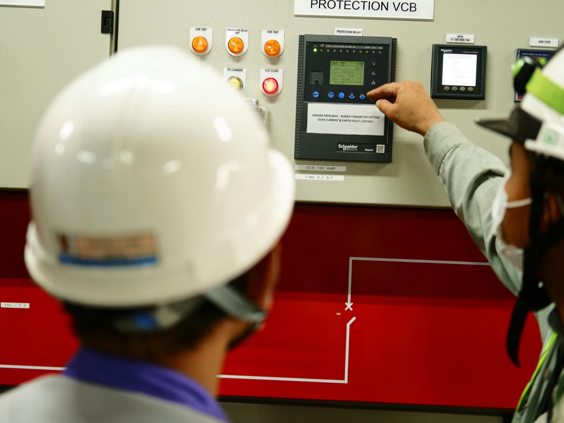 Engineers testing protection relay on switchgear panel